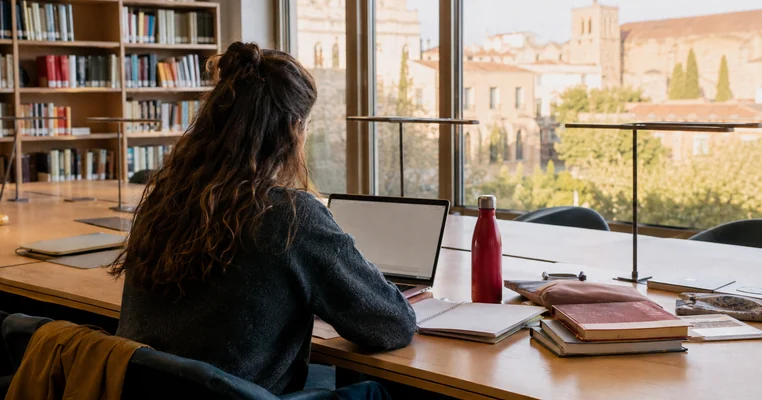 Estudiante universitaria consultando becas en una biblioteca de Cataluña